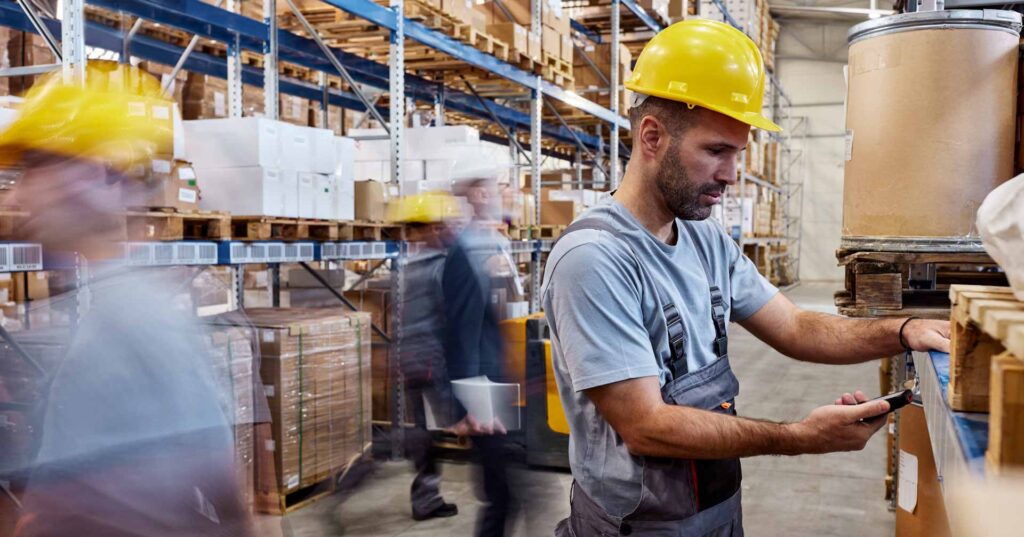 Warehouse worker using bar code reader while working in distribution warehouse. His colleagues are in blurred motion.