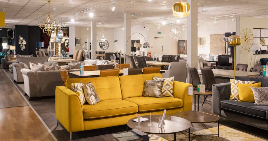 A wide angle of a furniture store with no people in. There is various different sofas and lamps and furniture on the shop floor for display purposes.