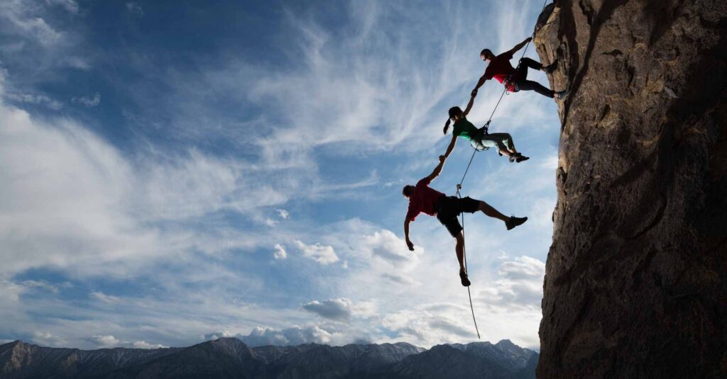 Three rock climbers helping one from falling in a dramatic setting