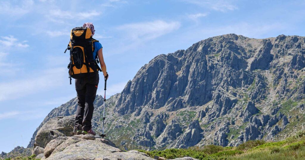 Rear view of a woman with backpack and poles looking at the mountain in front of her. Concept of overcoming