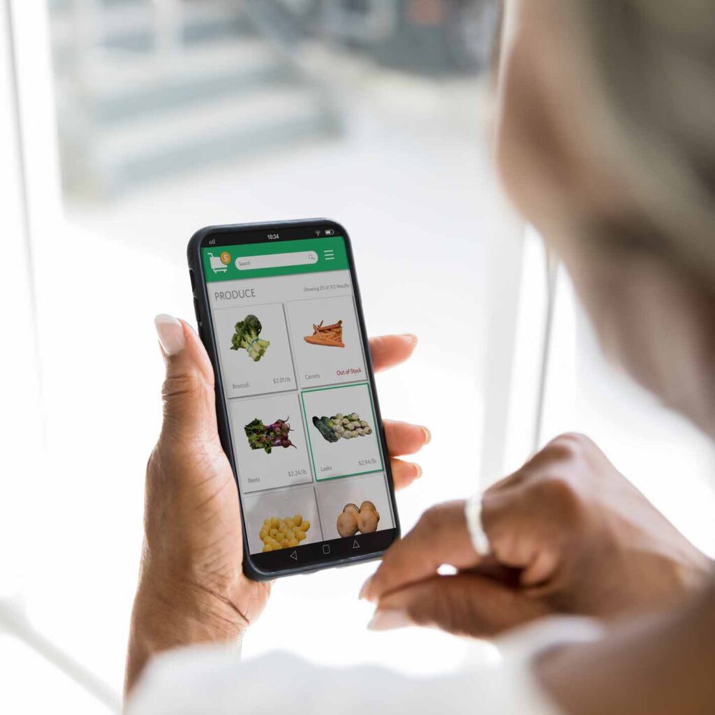 A woman uses a grocery delivery app on her smartphone. She is selecting fresh produce while using the app.