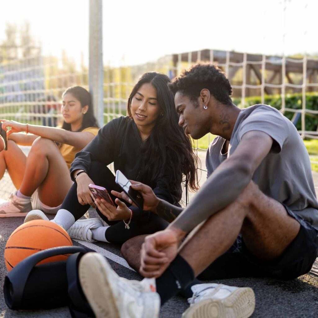 Urban young multi-ethnic basketball players using phone and chatting on the court