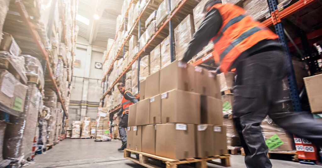 Motion blur of two men moving boxes in a warehouse.